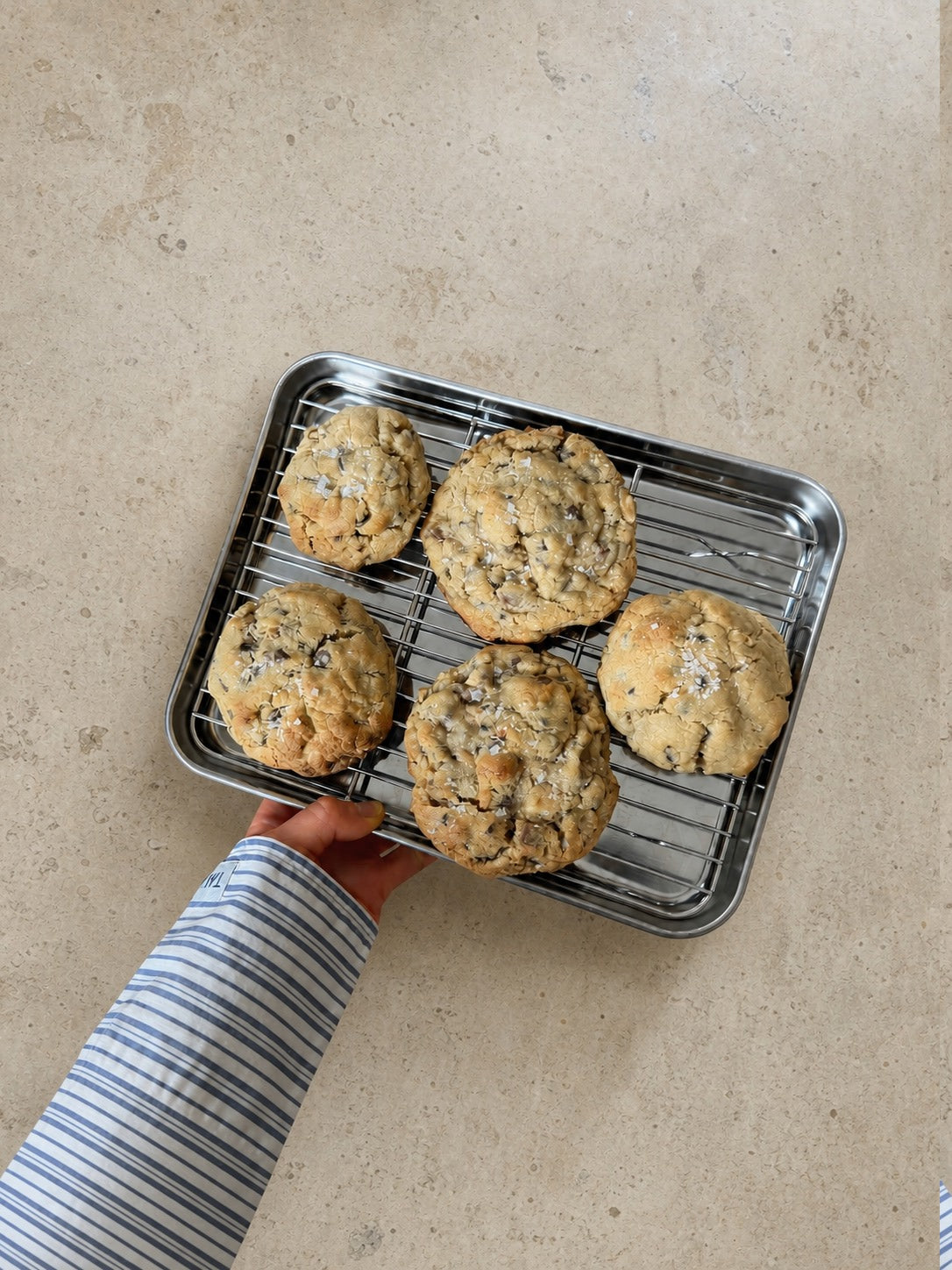 Five New York chocolate chip cookies on a tray held over a stone worktop.