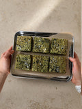 Six matcha brownies on a parchment-lined tray held over a stone worktop.