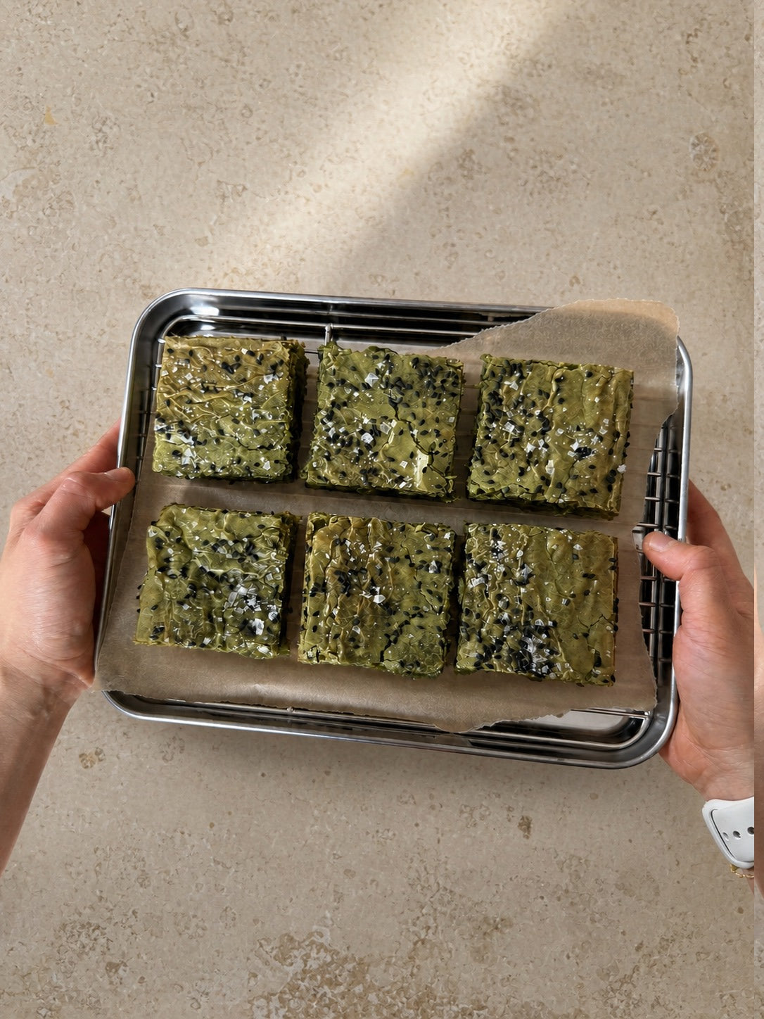 Six matcha brownies on a parchment-lined tray held over a stone worktop.
