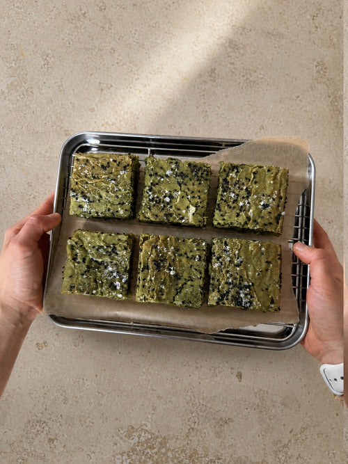 Six matcha brownies on a parchment-lined tray held over a stone worktop.